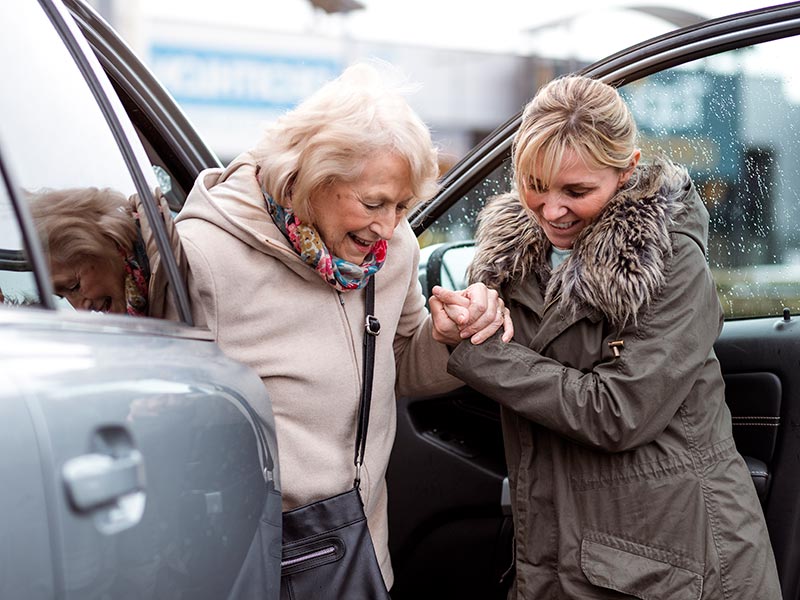 Younger woman helping older woman get out of a car